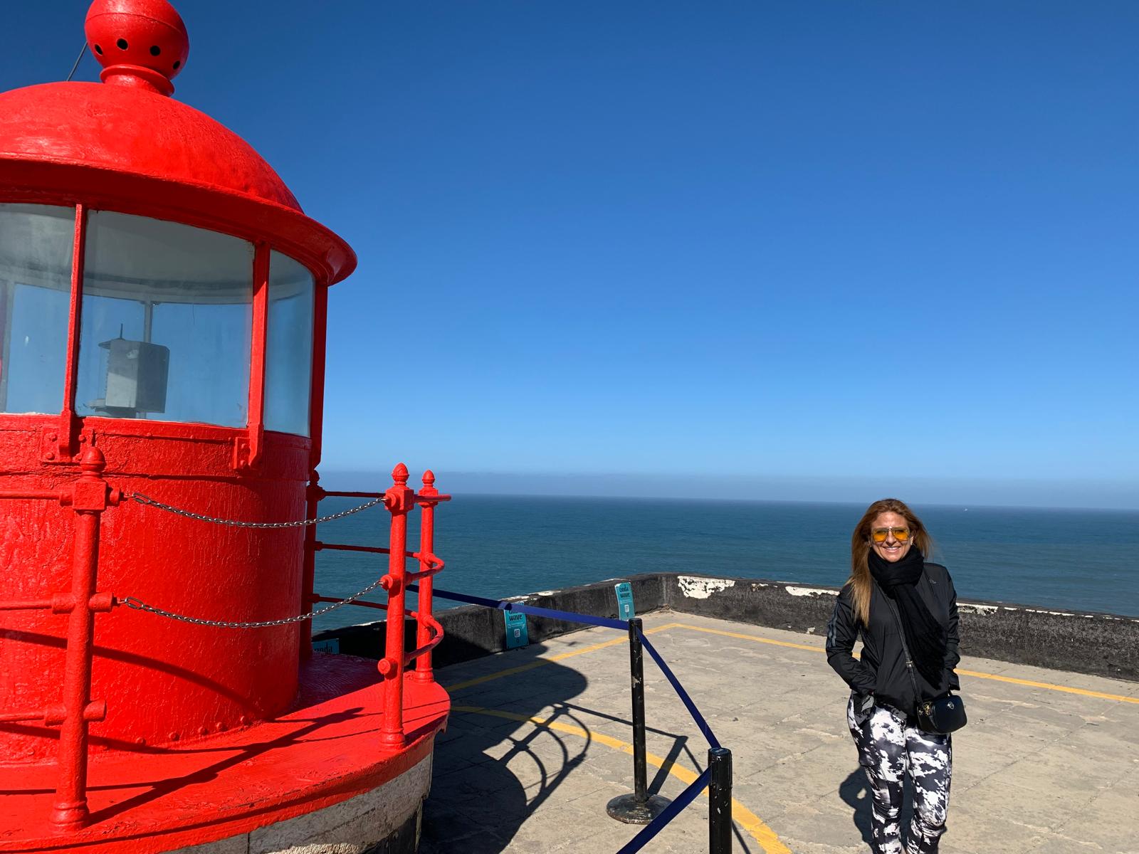 Marcella beside a red lighthouse overlooking the ocean