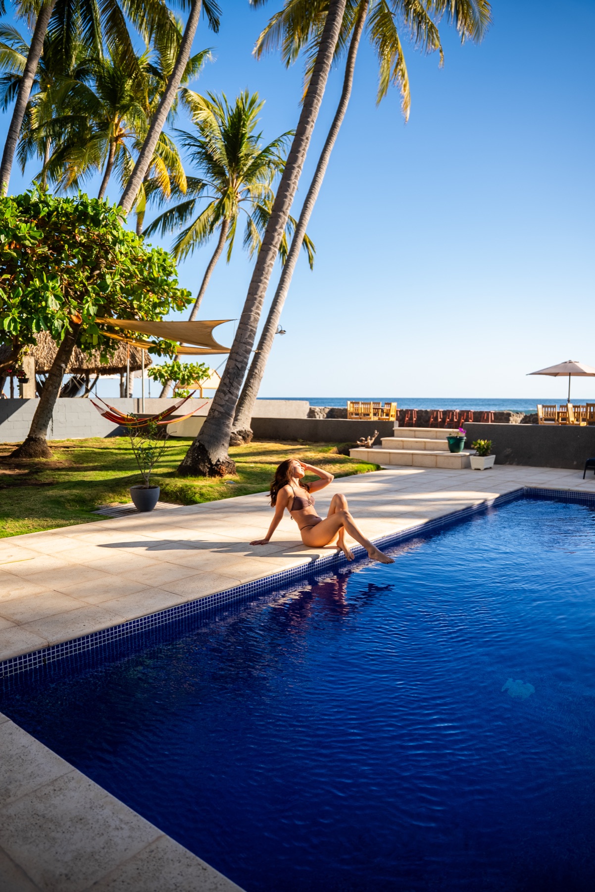 Guest relaxing beside the Casa Origen pool, with palms and the ocean beyond